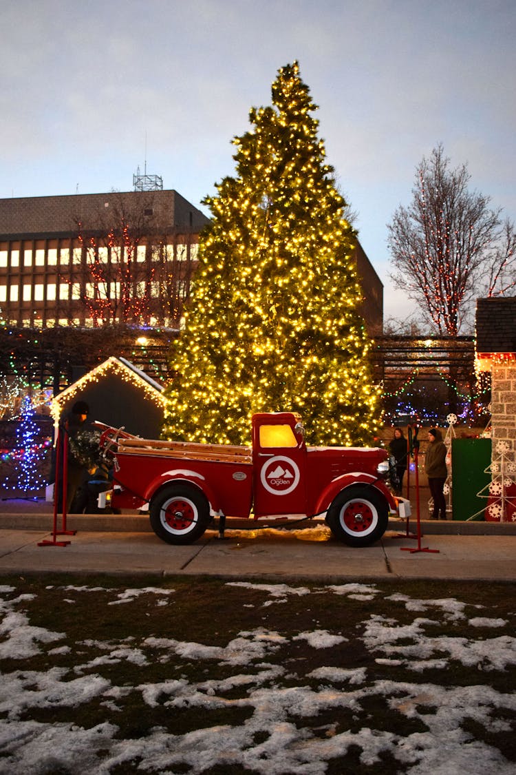 Red Truck By An Illuminated Christmas Tree At Dusk