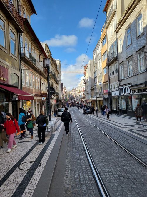 Free Lively street scene in downtown Porto with people walking along tram lines and shops. Stock Photo