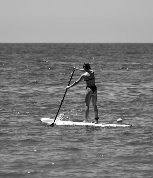 Grayscale Photo of Woman Paddle Boarding