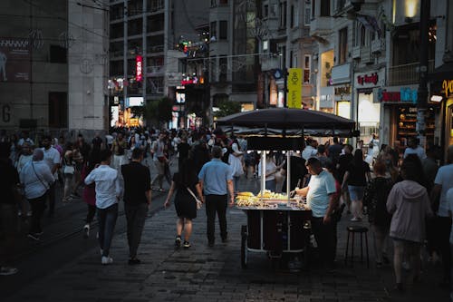 A Man Standing Beside a Food Cart on a Busy Street