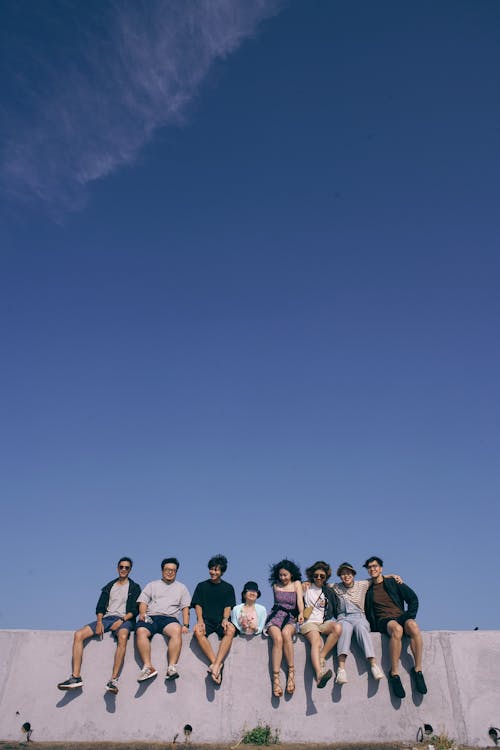 Group of Young People Sitting on a Wall under Blue Sky 