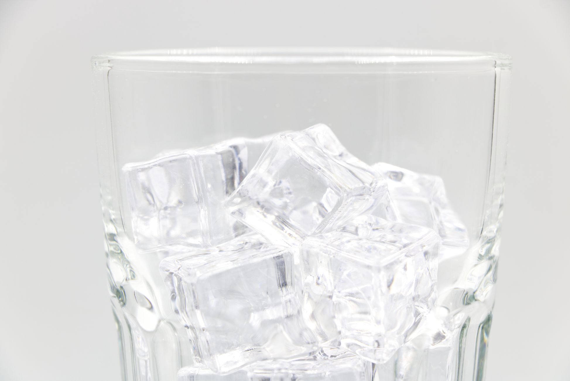 Close-up of transparent ice cubes inside a sparkling glass against a light background.