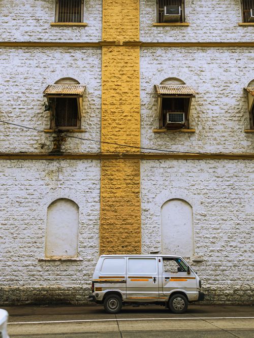 Free A white van parked in front of a rustic yellow and white building in Mumbai, India. Urban street scene. Stock Photo
