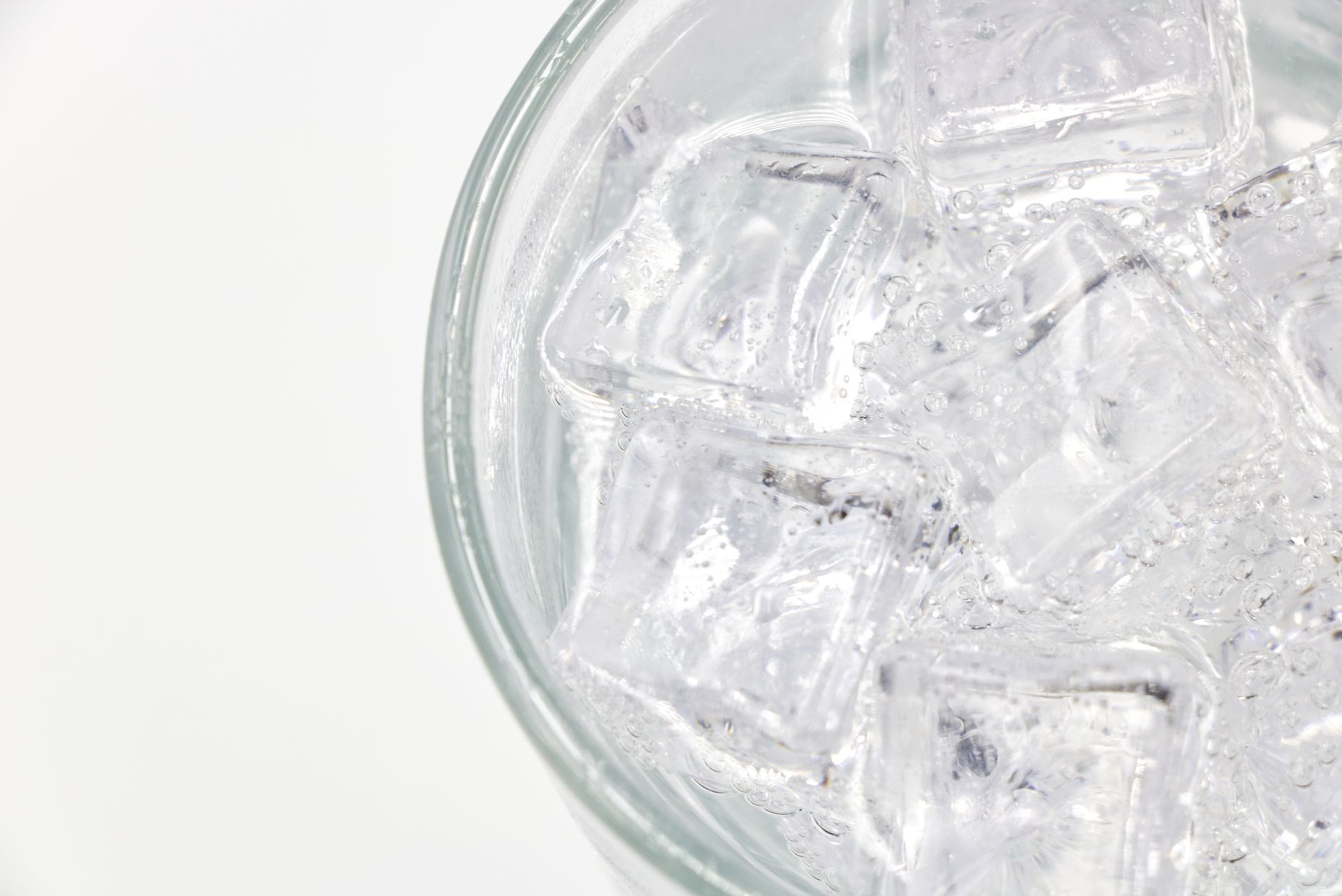Close-up of a glass filled with sparkling water and ice cubes on a white background.