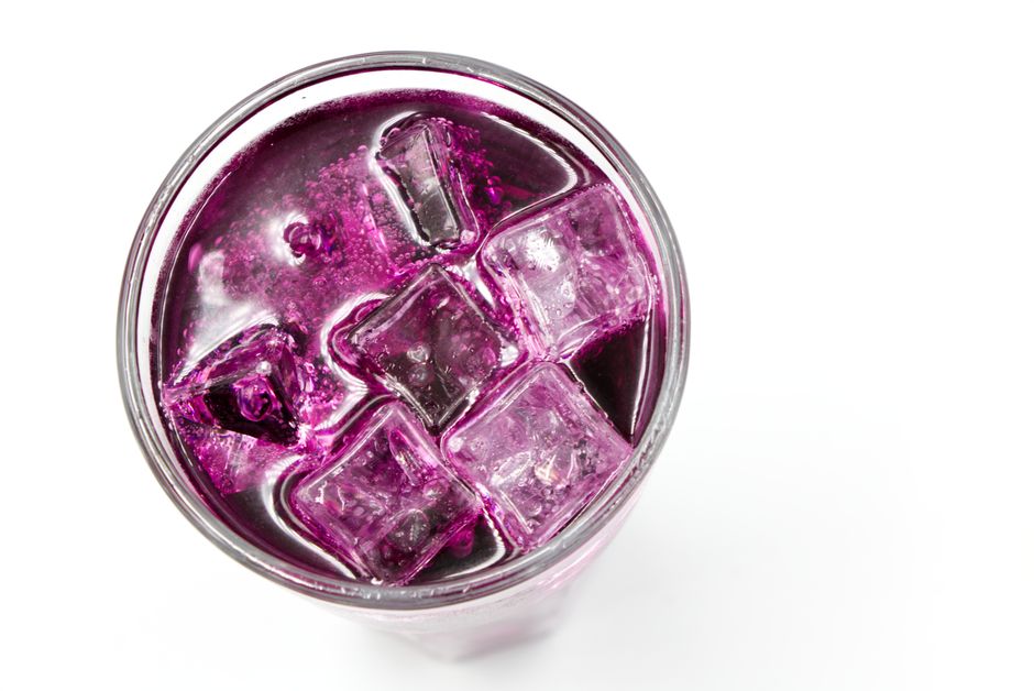 A glass of deep purple grape juice next to a small cluster of Concord grapes on a wood table