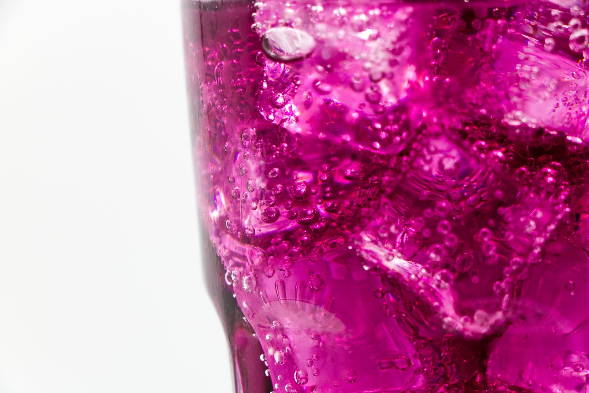A vibrant purple refreshing drink with ice cubes and bubbles in a glass close-up.