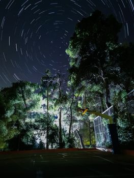 Captivating star trails swirling over a basketball court, surrounded by tall trees at night.
