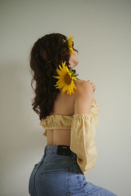 Brunette woman in stylish outfit holding sunflowers, creating a serene and artistic portrait.