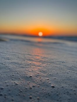 A tranquil sunset over a beach with sea foam in the foreground, creating a calming seascape.