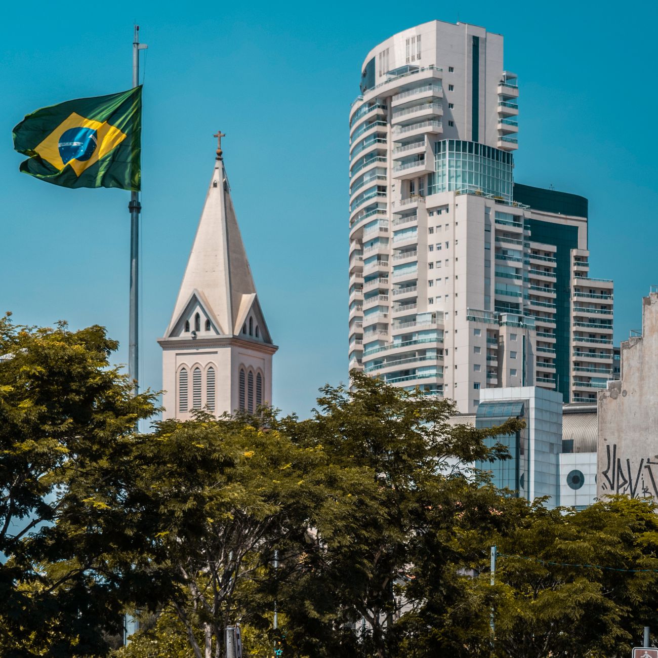 Skyline view in São Paulo featuring Brazilian flag, church, and modern architecture.