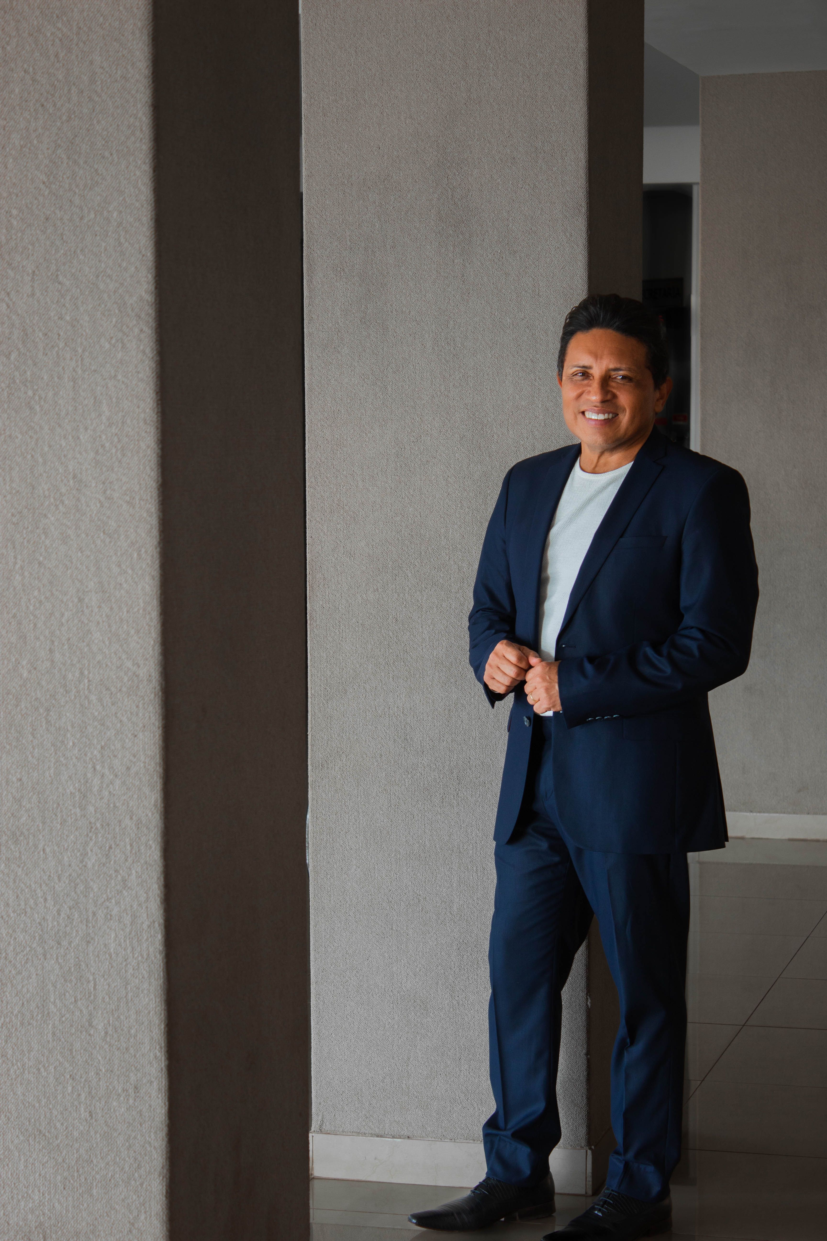 Confident businessman in a blue suit standing indoors with a smile, offering professional demeanor.