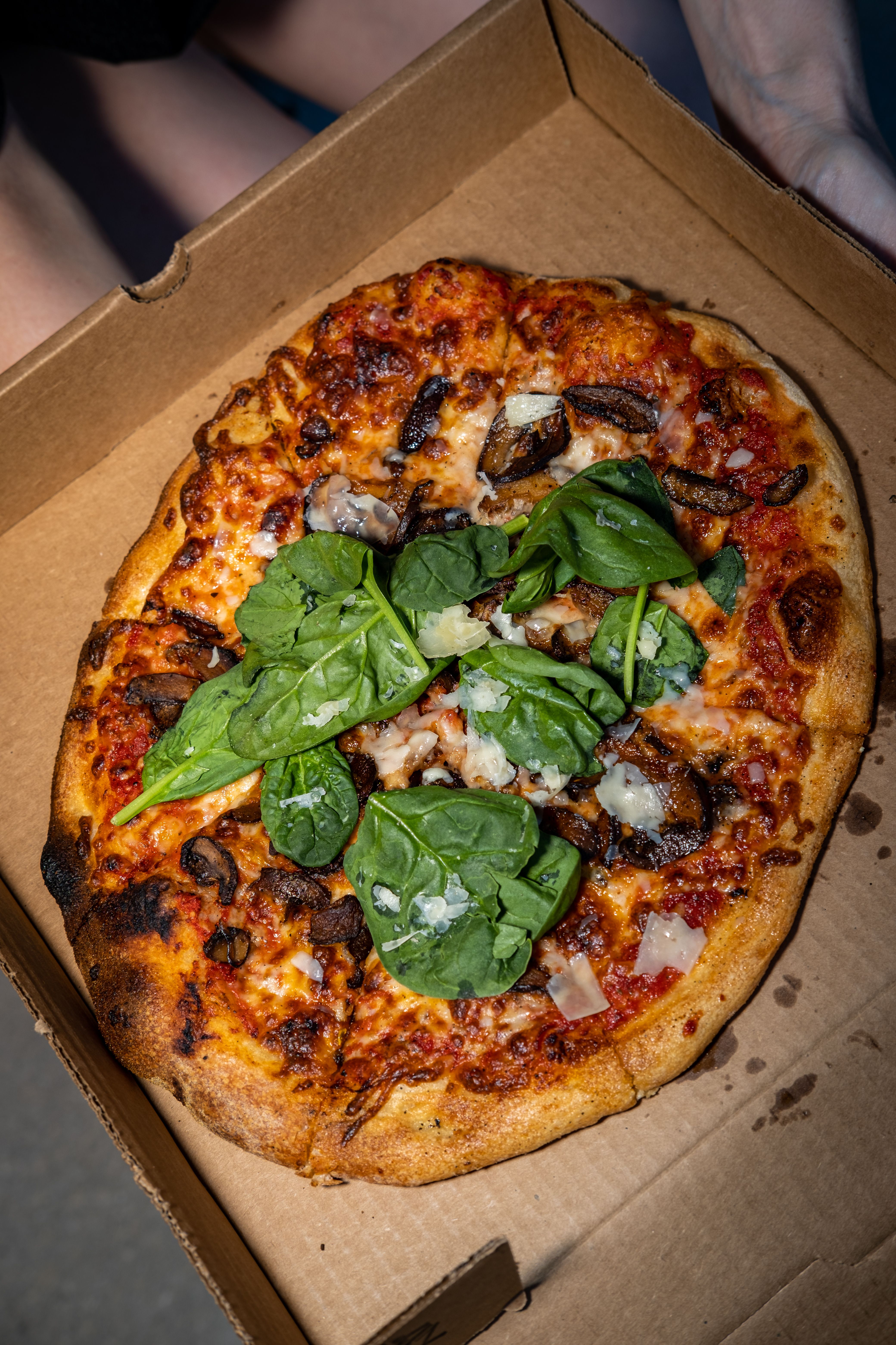 A fresh pizza topped with spinach and mushrooms in a cardboard box, perfect for a tasty meal.