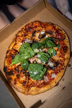 A fresh pizza topped with spinach and mushrooms in a cardboard box, perfect for a tasty meal.