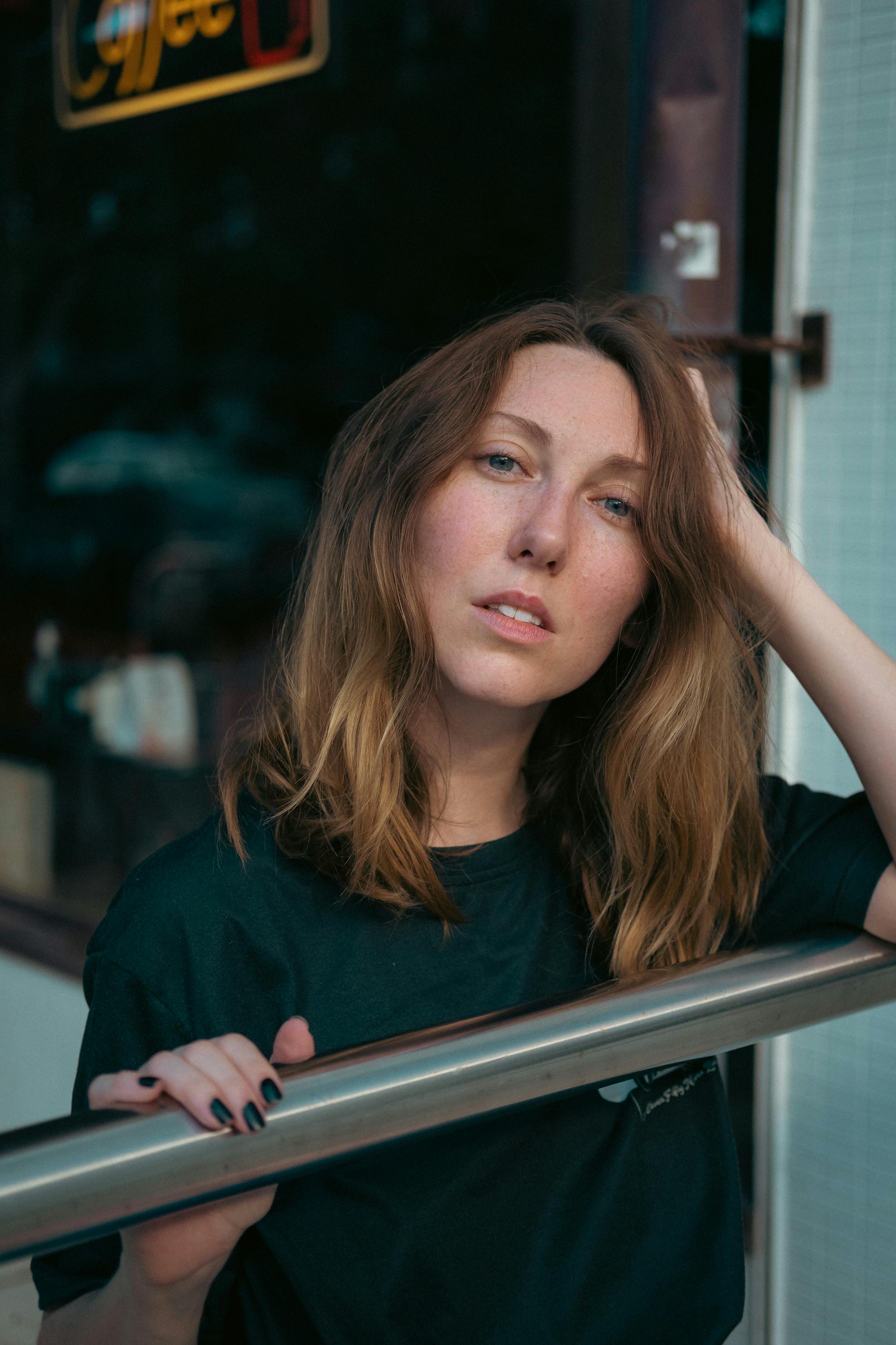 A woman with long hair leans on a railing outside a cafe, exuding a relaxed vibe.