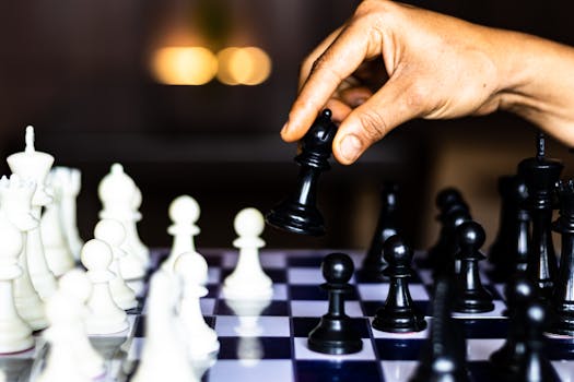 A focused close-up of a hand moving a black chess piece during a game.