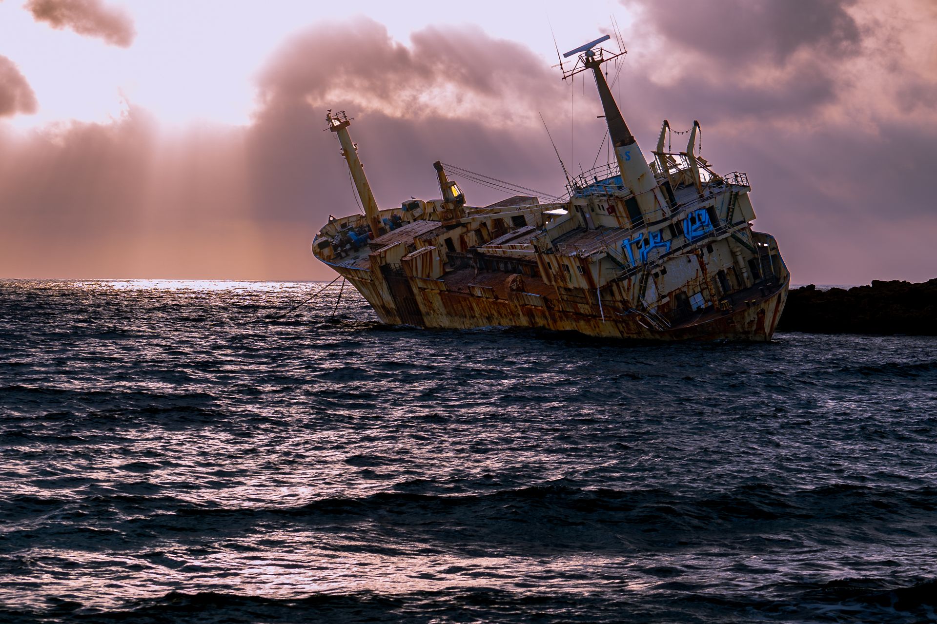 Captivating view of a rusty shipwreck against a dramatic sunset, showcasing waves and ocean beauty.