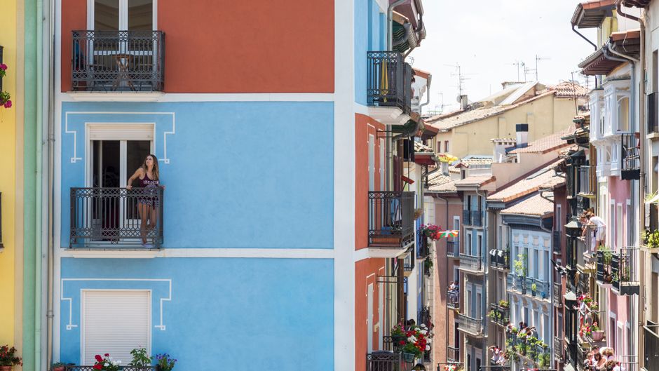 Paisaje urbano vibrante con una mujer en un balcón, edificios urbanos coloridos a la luz del día.