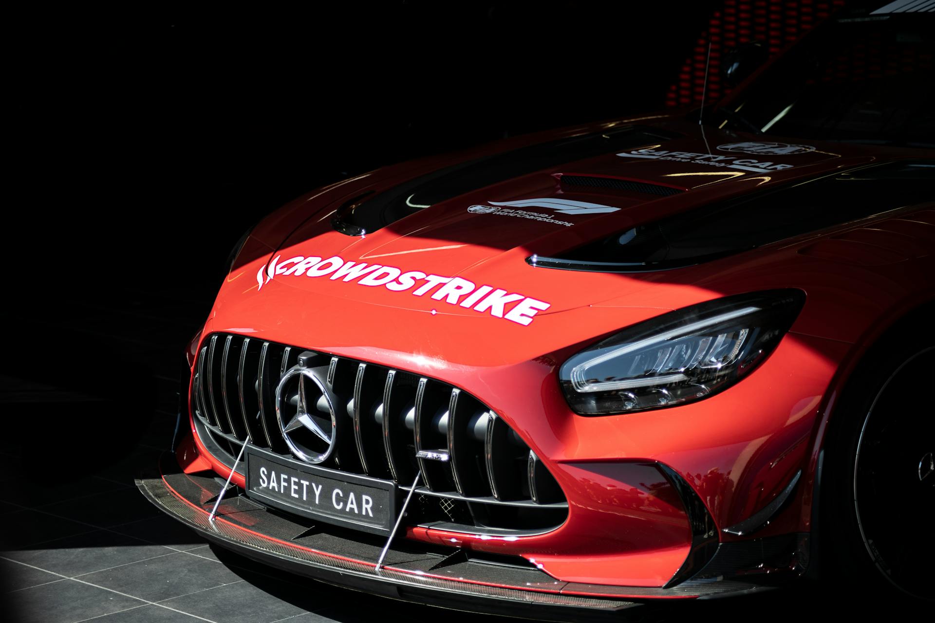 Close-up of a red Mercedes-Benz AMG GT safety car showcasing bold CrowdStrike branding in a dimly lit garage.