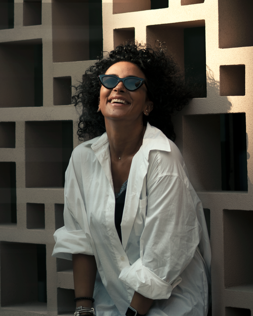 Free Woman in a white blouse, smiling with curly hair and sunglasses against a patterned wall in Istanbul. Stock Photo