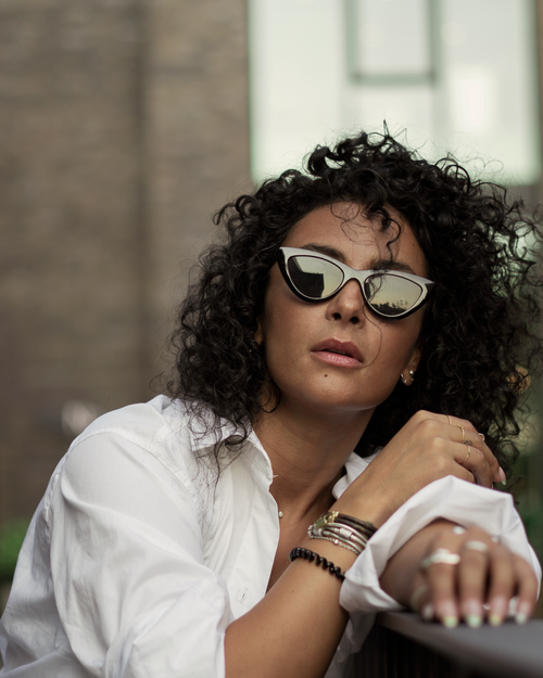 Free Chic woman with curly hair in sunglasses and white shirt posing outdoors. Stock Photo