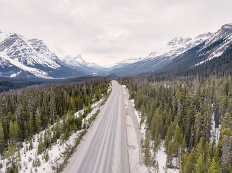 A breathtaking aerial view of a snowy mountain road in Alberta, Canada surrounded by forests.