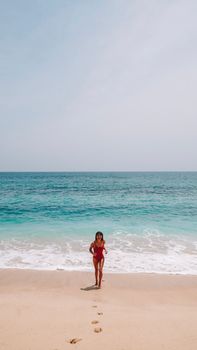 A woman enjoys a sunny day at the beach, walking towards the ocean in a red bikini.