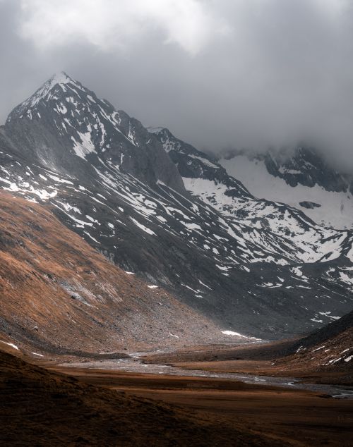 Free Snow-covered mountains in Tirol, Austria with dramatic cloudy skies. Perfect for winter-themed content. Stock Photo