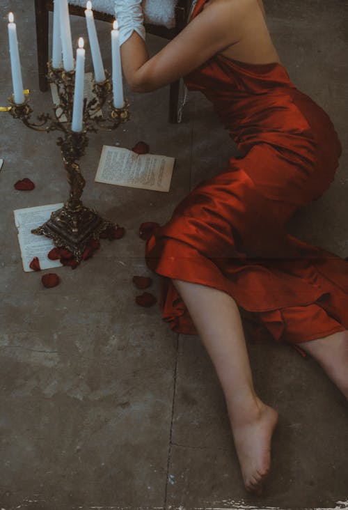 Woman Wearing Red Silk Dress Lying Down on a Concrete Floor with a Chandelier