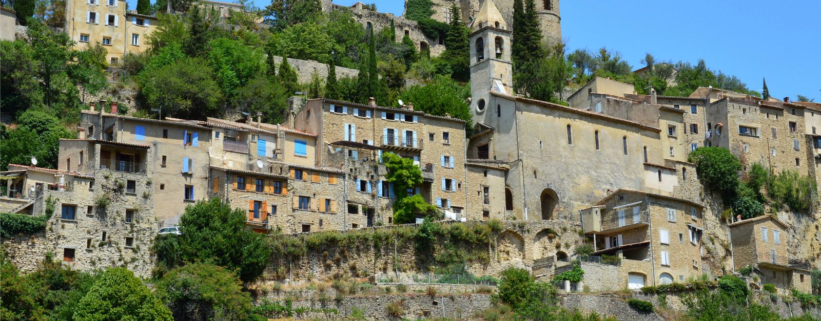 Scenic view of the historic Montbrun-les-Bains village with stone buildings and lush greenery.