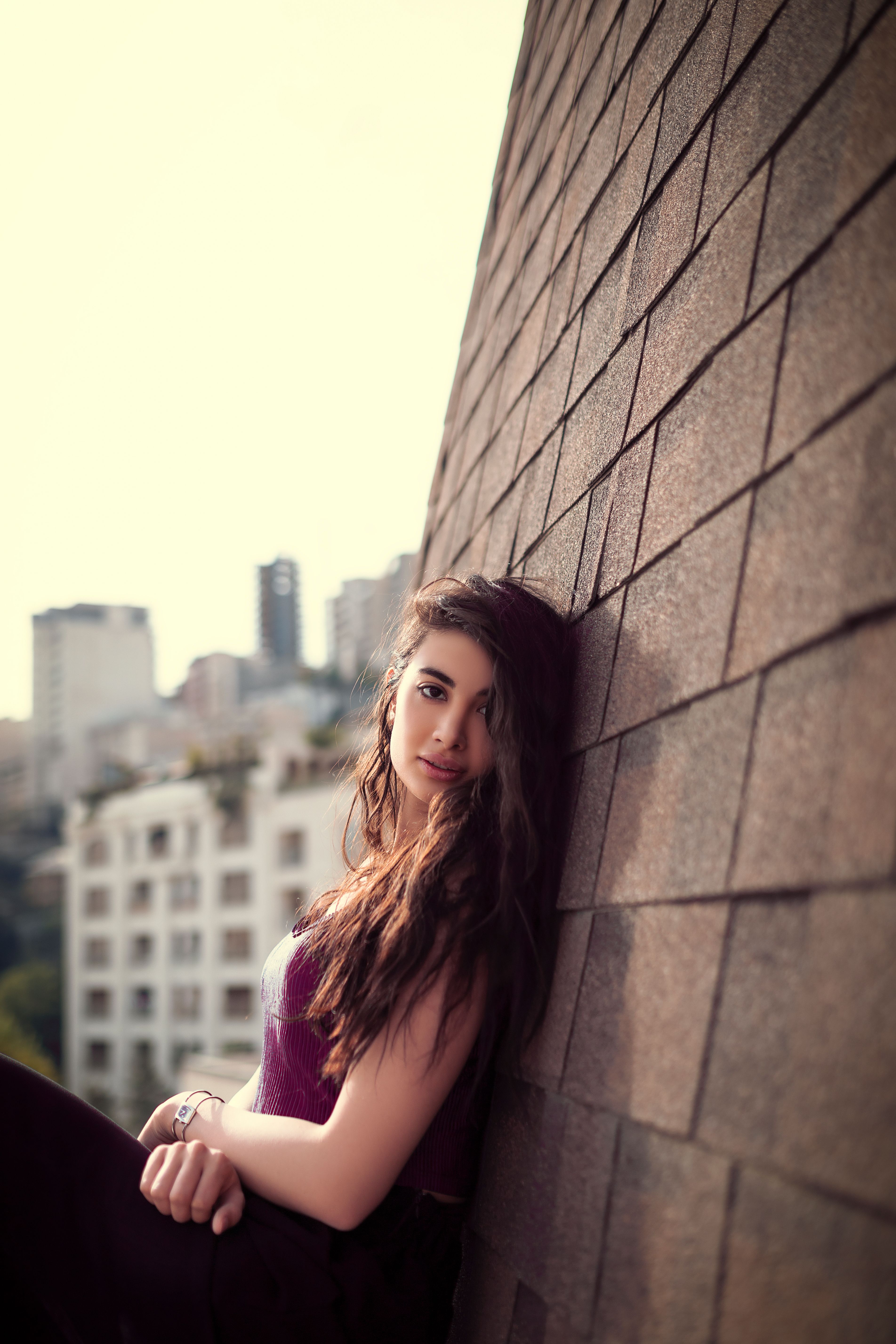Fashionable woman leaning against a wall with a cityscape backdrop.