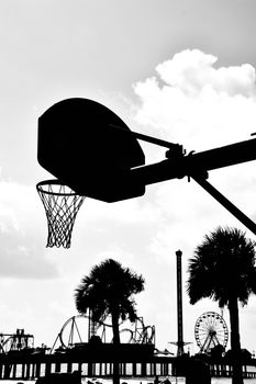 Silhouette of a basketball hoop with roller coasters in the background, taken in Texas.