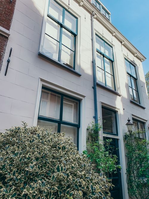 Free Beautiful three-story townhouse in Amsterdam, showcasing elegant traditional windows and lush greenery. Stock Photo