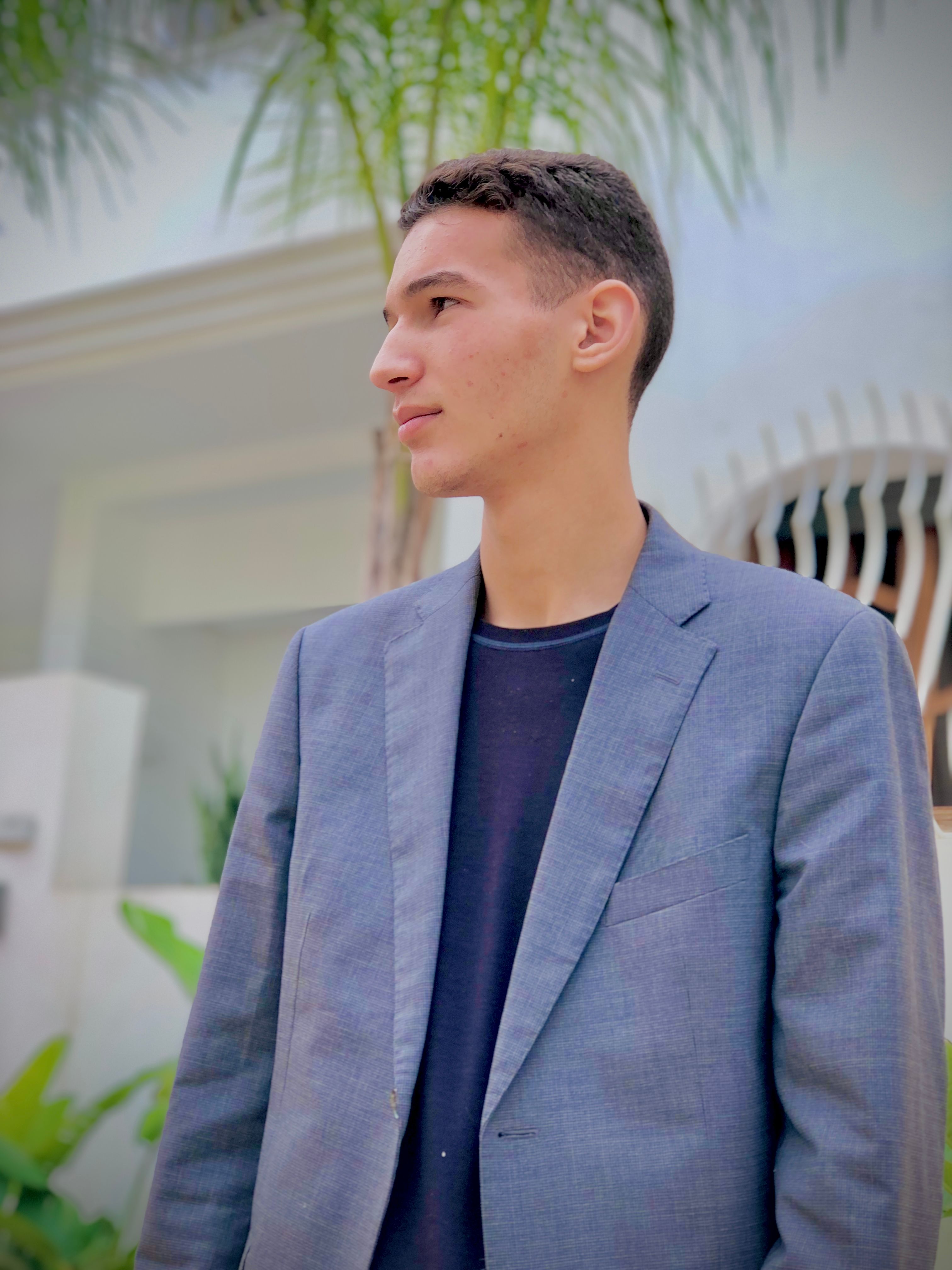 A young man in a blue blazer poses outdoors in Fez, Morocco, exuding confidence.