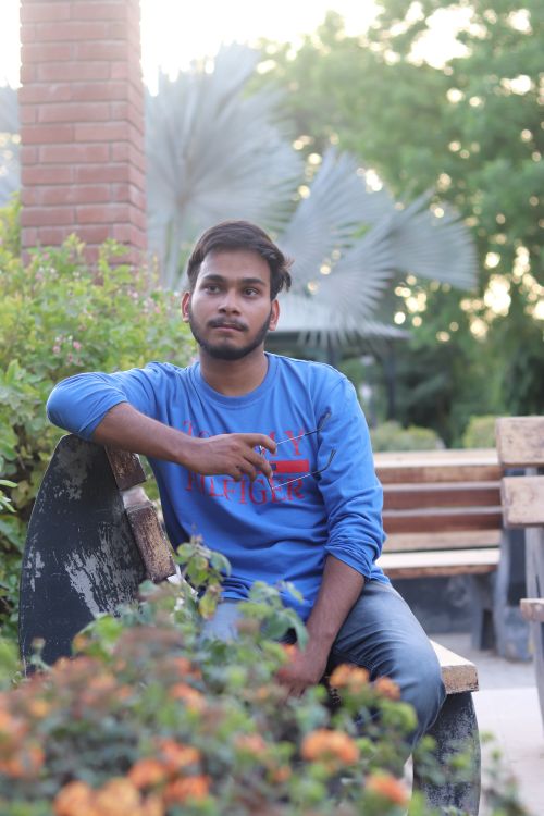 Free Casual portrait of a young man sitting on a park bench in a serene garden. Stock Photo