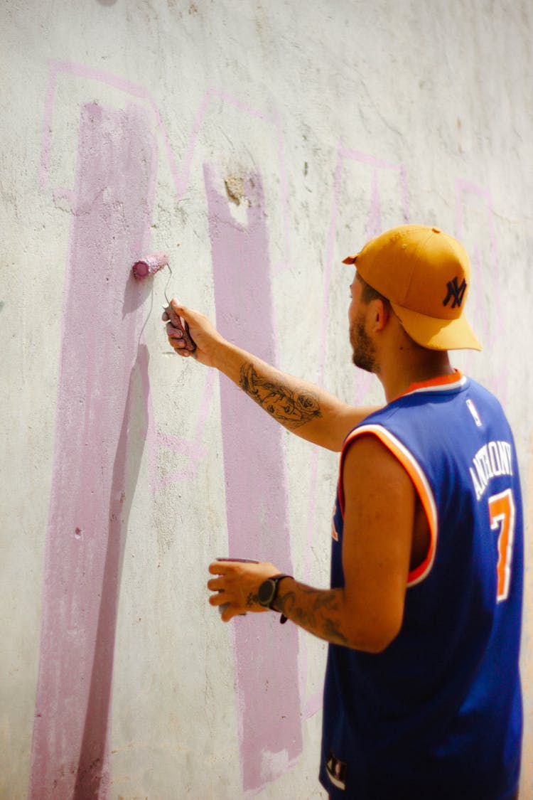 A Tattooed Man In A Cap Painting A Concrete Wall