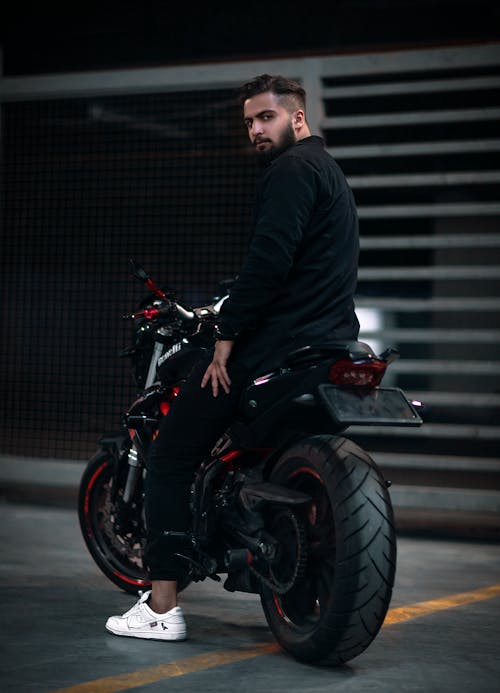 A Man in Black Jacket and Pants Riding a Motorcycle while Looking Over Shoulder