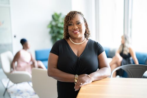 Free Portrait of a smiling woman in a black shirt standing indoors, with people in the blurred background. Stock Photo