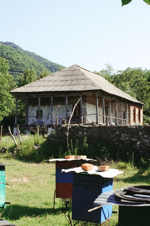 Free A scenic view of colorful beehives in front of an old, rustic house surrounded by lush greenery and hills. Stock Photo