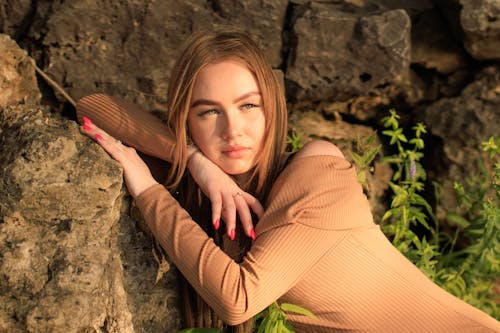 A Beautiful Woman in Brown Long Sleeves Leaning on the Rock
