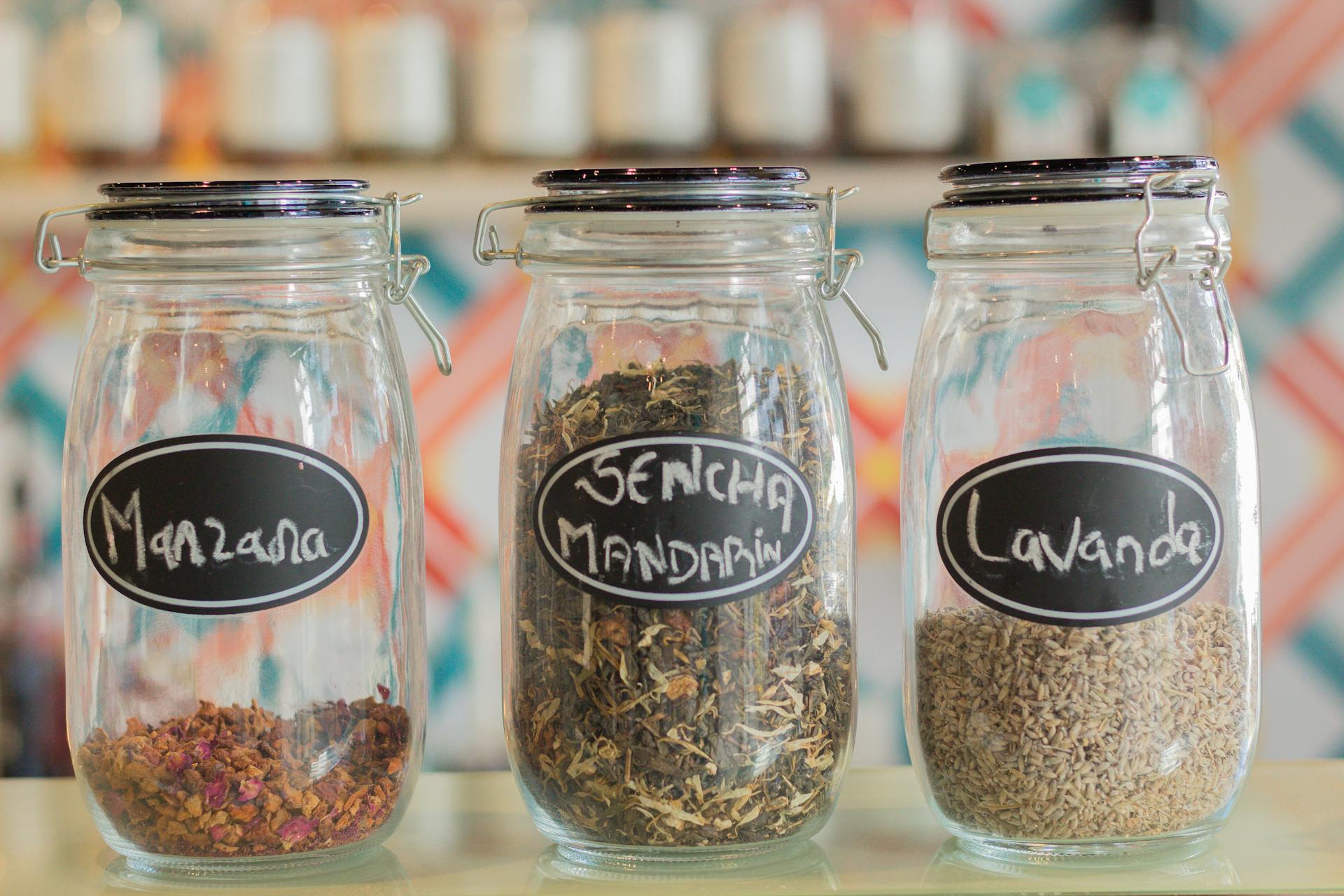 Three glass jars labeled with herbs and spices including manzana, sencha mandarin, and lavanda.