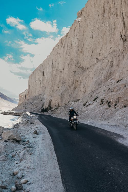 Free A motorcyclist travels on a scenic road by rocky cliffs under a clear blue sky. Stock Photo