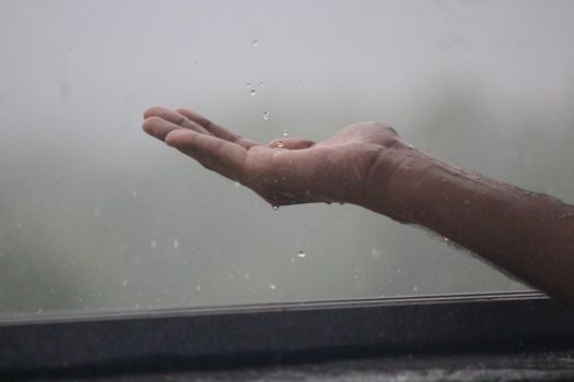 Close-up of a hand reaching out to catch raindrops during a rain shower in Mangaluru, India.