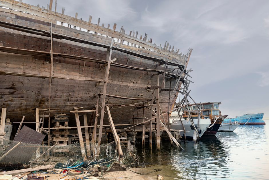 Aged wooden ship and various boats docked at a harbor in Dubai, UAE.
