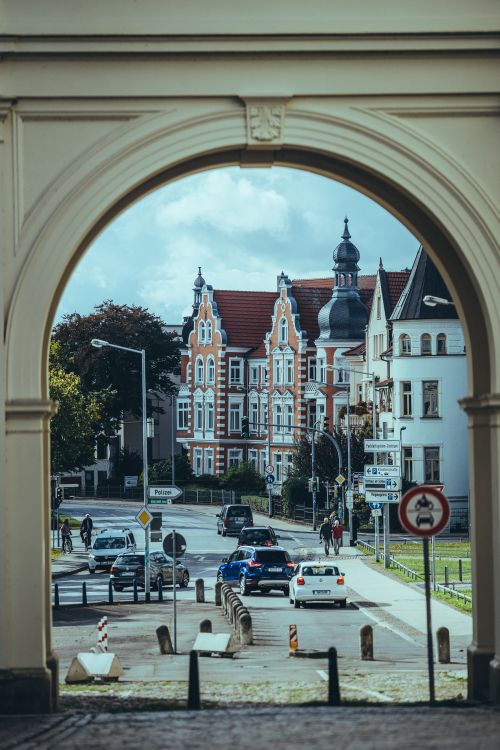 Free View of picturesque European architecture framed by an arch, featuring lively street activity. Stock Photo
