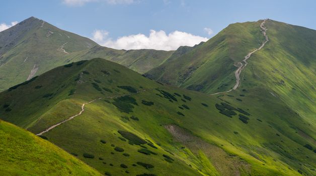 Breathtaking view of green mountains with winding trails under a blue sky.