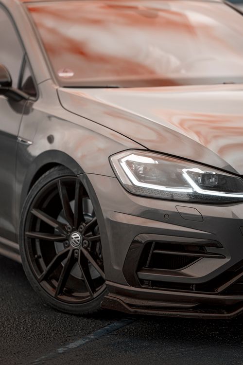 Free Front view of a luxury car showcasing its sleek design and contemporary style on a wet street. Stock Photo