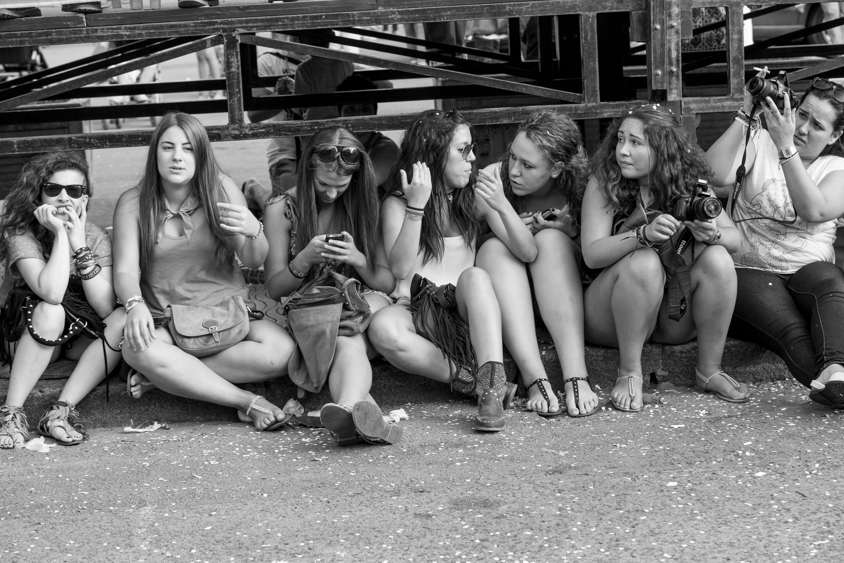 Candid grayscale photo of young women sitting together with cameras outdoors.