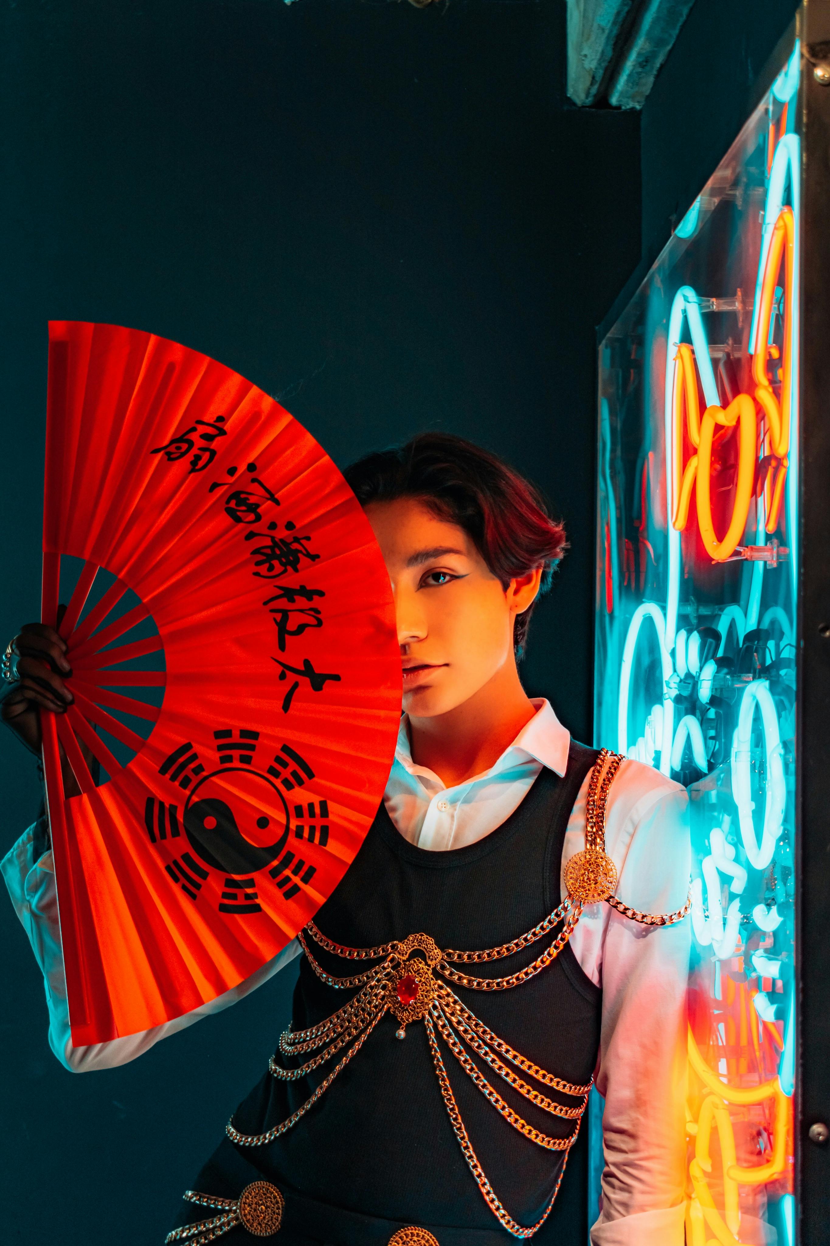 Free A person poses with a red Asian fan beside neon lights, embodying traditional and modern fusion. Stock Photo