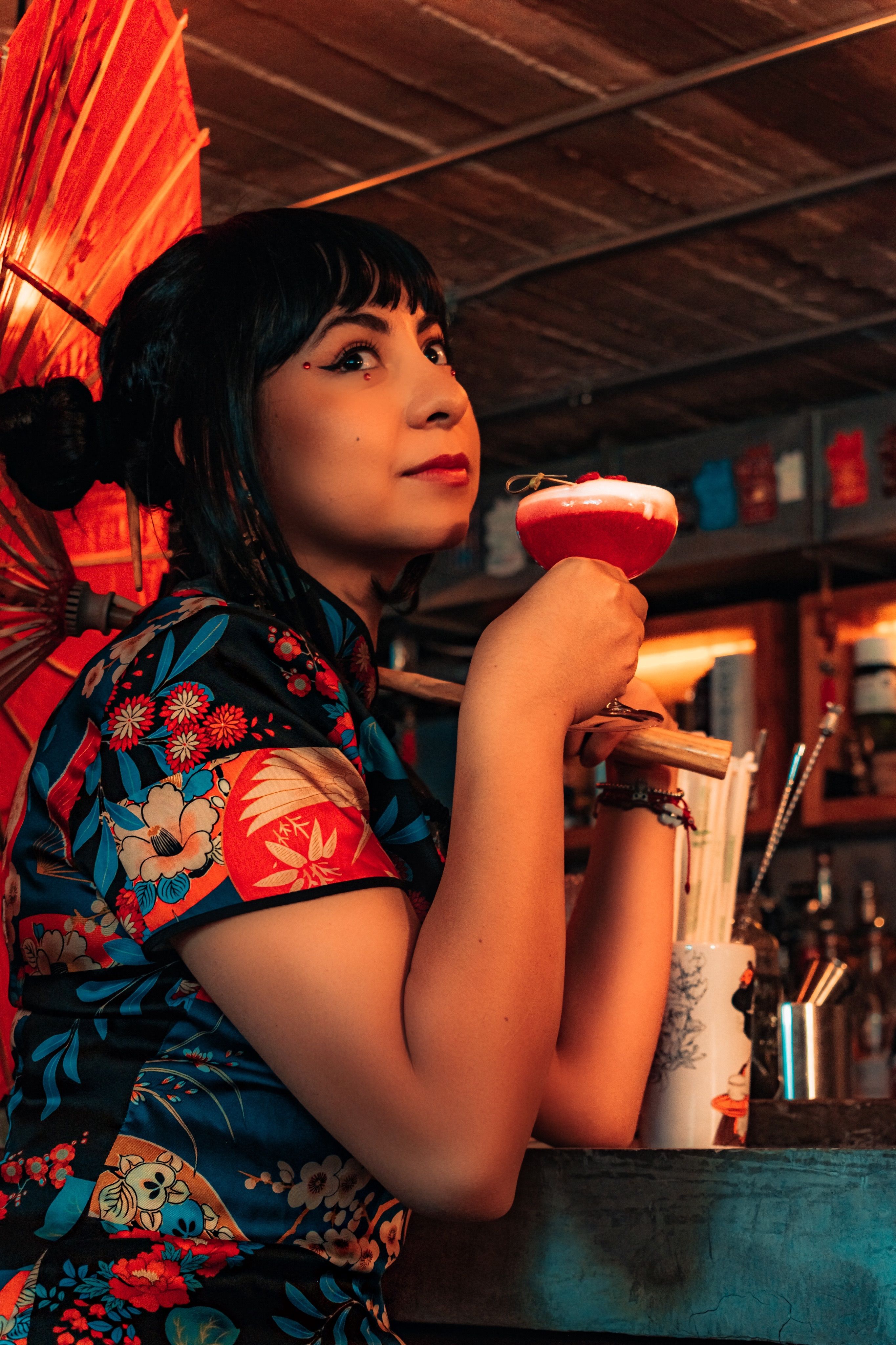 A fashionable woman with a cocktail in a vibrant bar setting.