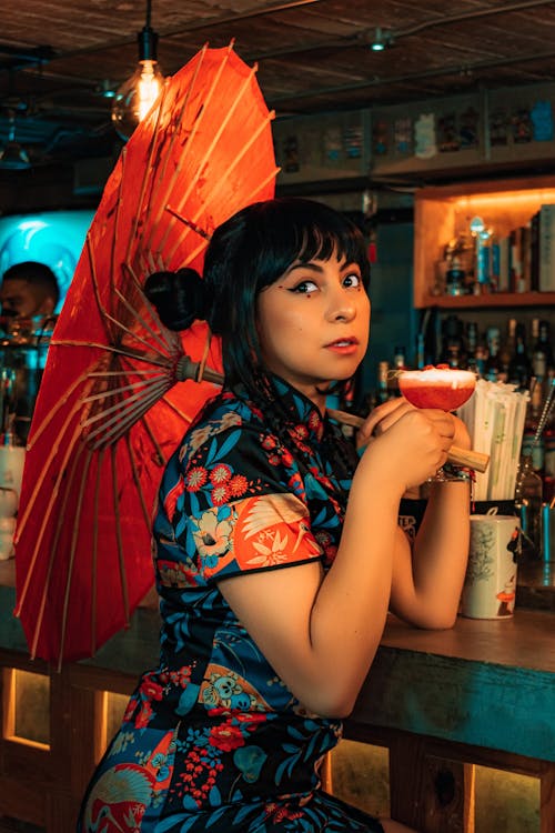 Woman in Red and White Floral Dress Drinking from Clear Drinking Glass